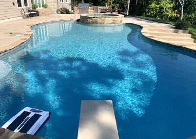Inground pool and spa equipped with diving board and steps built in to pool deck